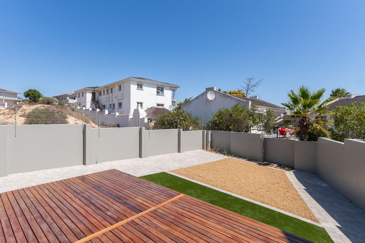 A private rear garden featuring a timber deck, paved areas, and low-maintenance landscaping enclosed by high perimeter walls with electric fencing.