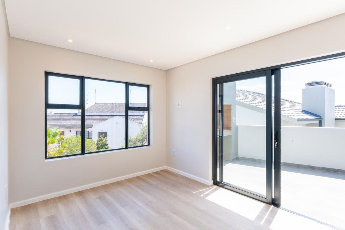 Bright and modern bedroom featuring light wood-look flooring, large black-framed windows, and sliding glass doors opening onto a private balcony.