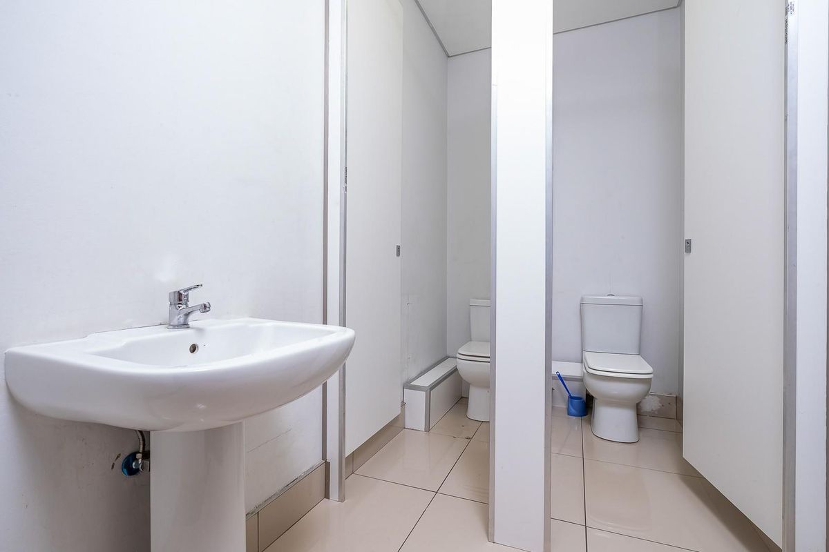 A functional office restroom featuring a pedestal sink and two private toilet stalls with tiled flooring and partition walls.