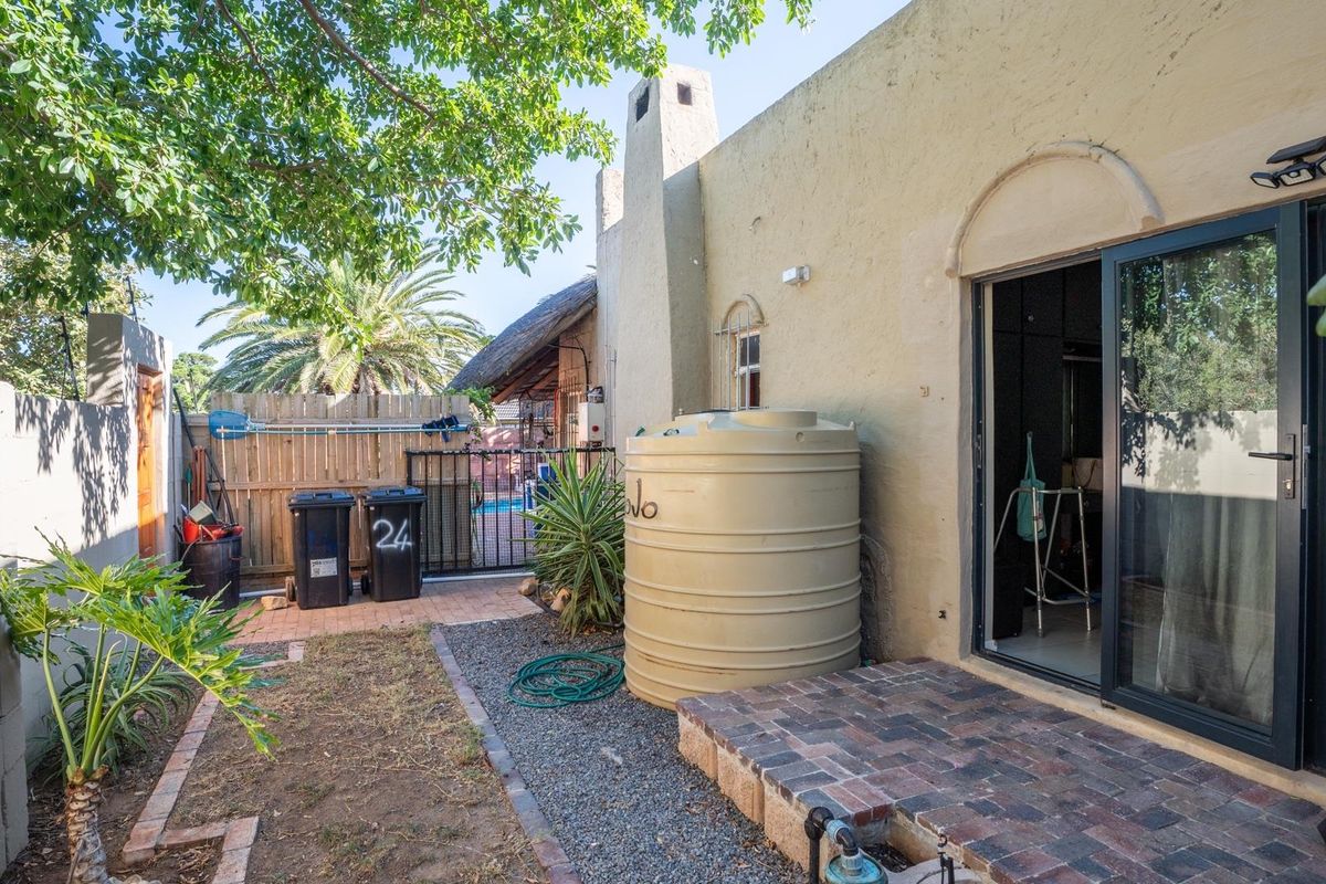A rear exterior view featuring a brick patio, a water storage tank, a chimney stack, and sliding glass door access to the home.