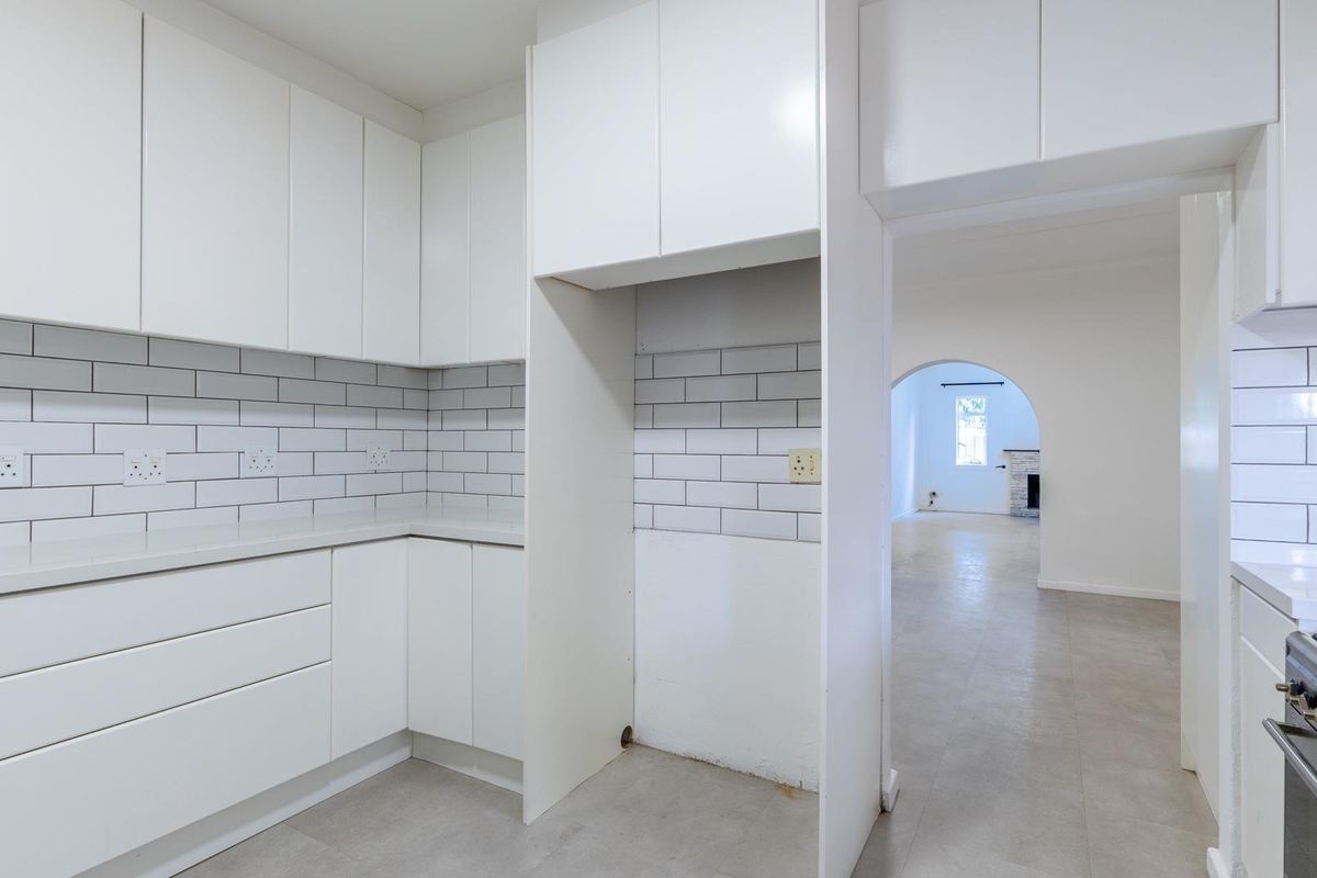Modern kitchen featuring white cabinetry, subway tile backsplash, stone countertops, and a built-in gas stove, leading into an adjacent living area with an arched doorway.