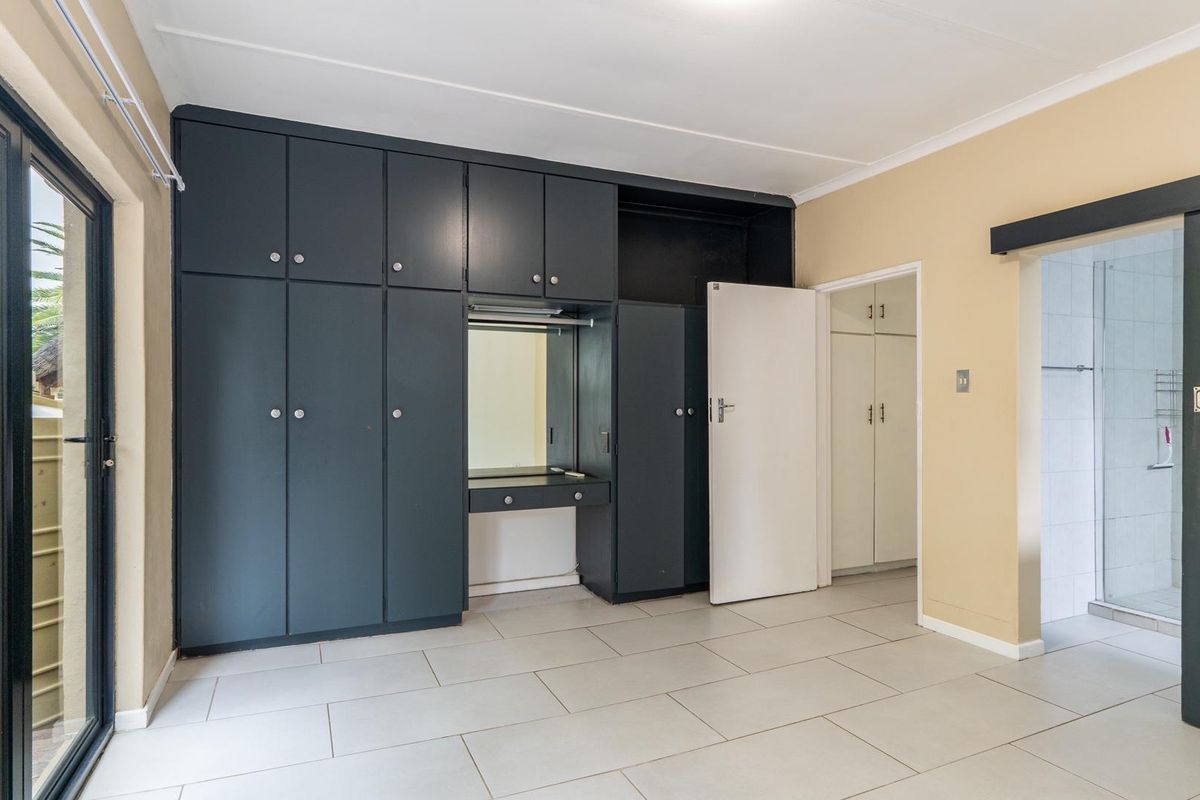 Bedroom featuring built-in dark cabinetry with integrated vanity, tiled flooring, and direct access to an en-suite bathroom and outdoor area.