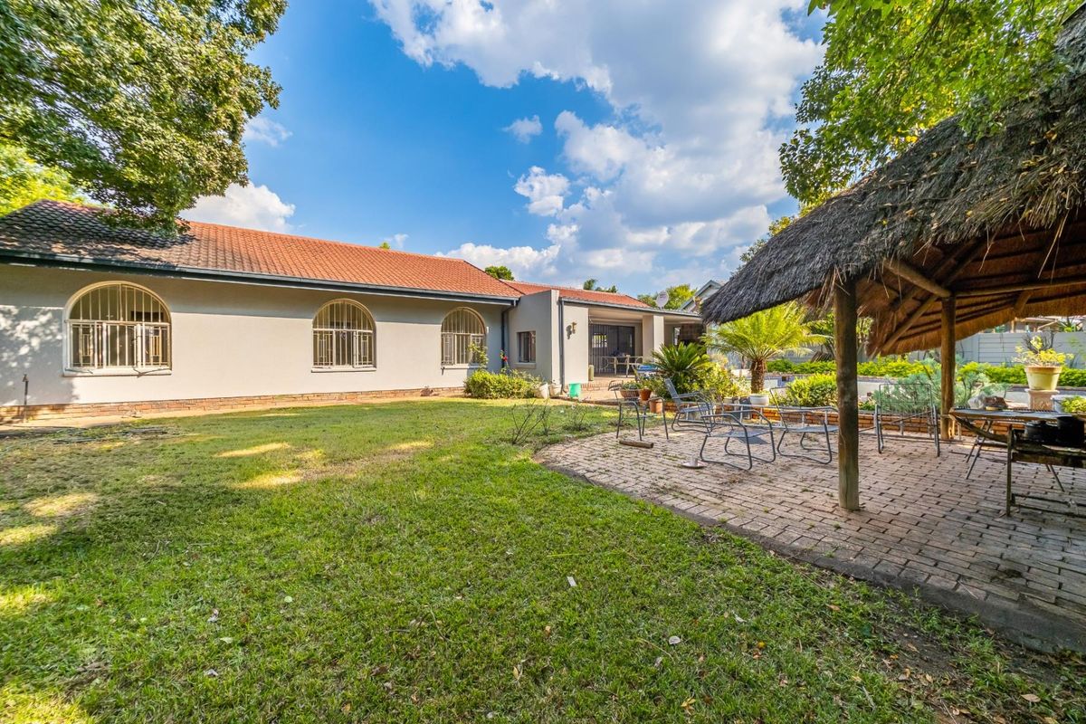 Spacious rear garden featuring a lawn, paved patio area, and a traditional thatched lapa structure overlooking the main house exterior.