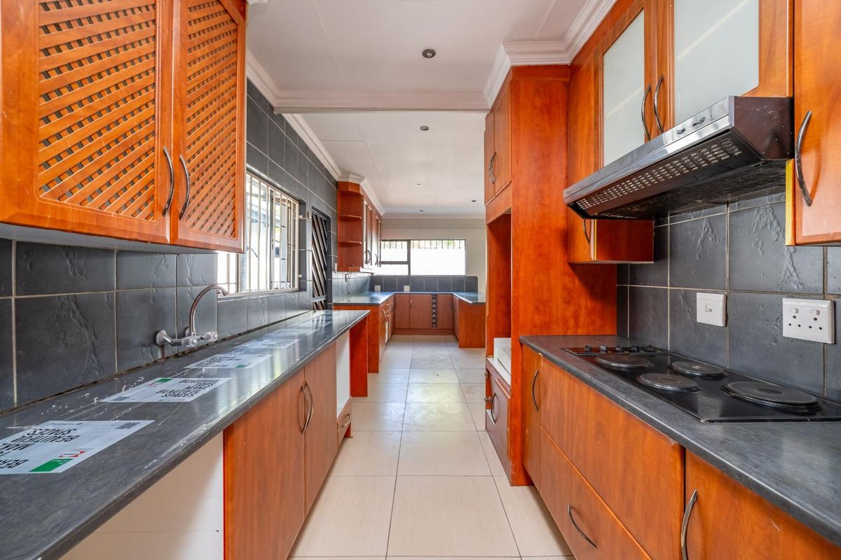 A galley-style kitchen featuring wooden cabinetry, dark stone-look countertops, a built-in electric hob, and an extractor fan with tiled splashbacks.