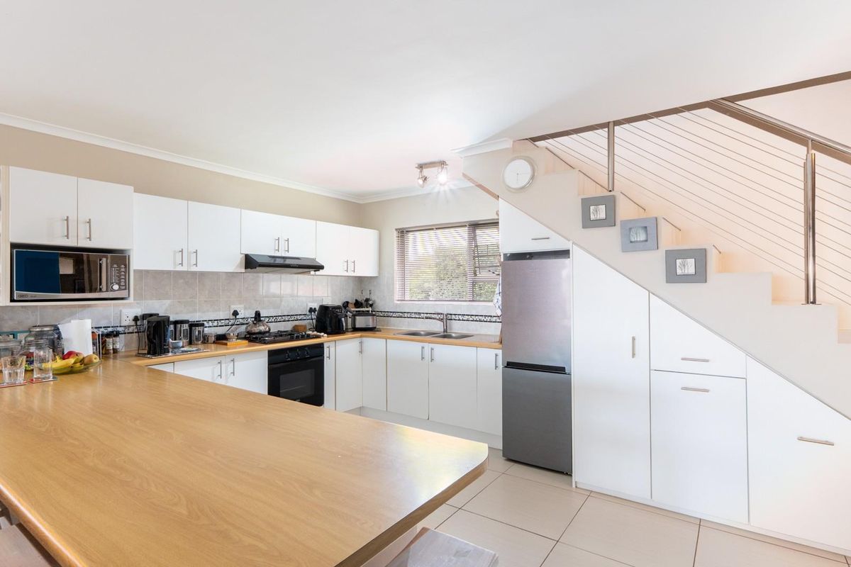 A functional kitchen featuring white cabinetry, a wooden breakfast bar, built-in oven, hob, and integrated storage space beneath the staircase.