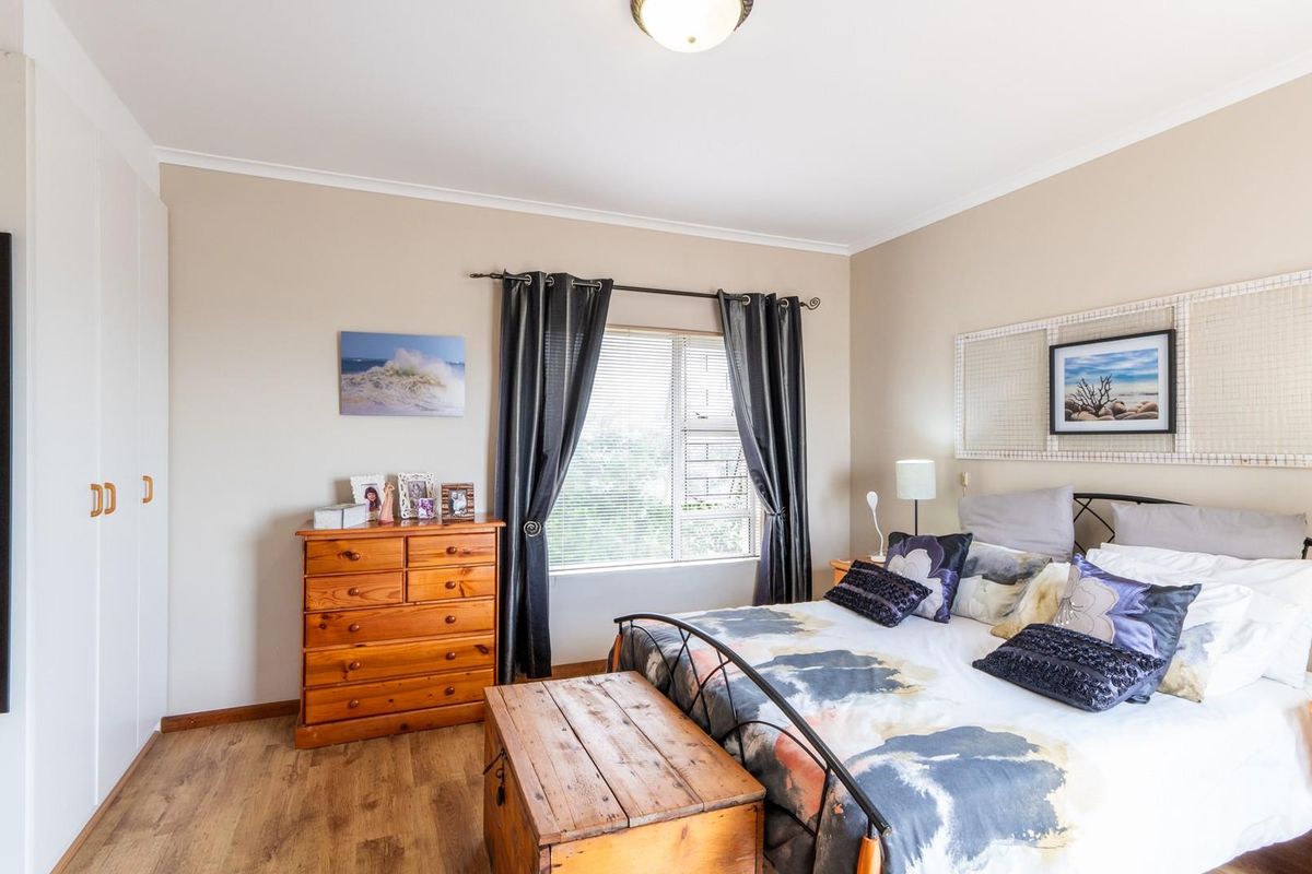 A well-maintained bedroom featuring built-in wardrobes, wood-look flooring, and a window with curtain treatments.