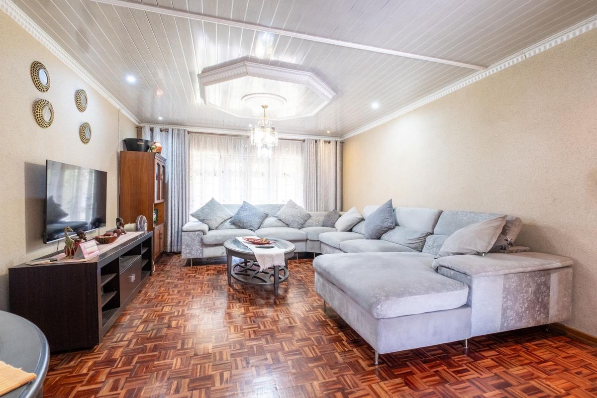 A comfortable living room featuring classic parquet wood flooring, a decorative coffered ceiling with a central chandelier, and large windows allowing natural light.