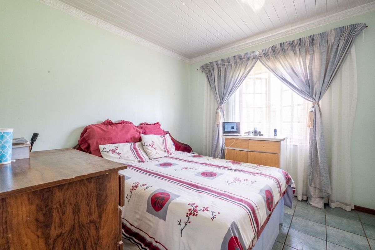 A functional bedroom featuring tiled flooring, a white tongue-and-groove ceiling, and a window with curtain treatments.