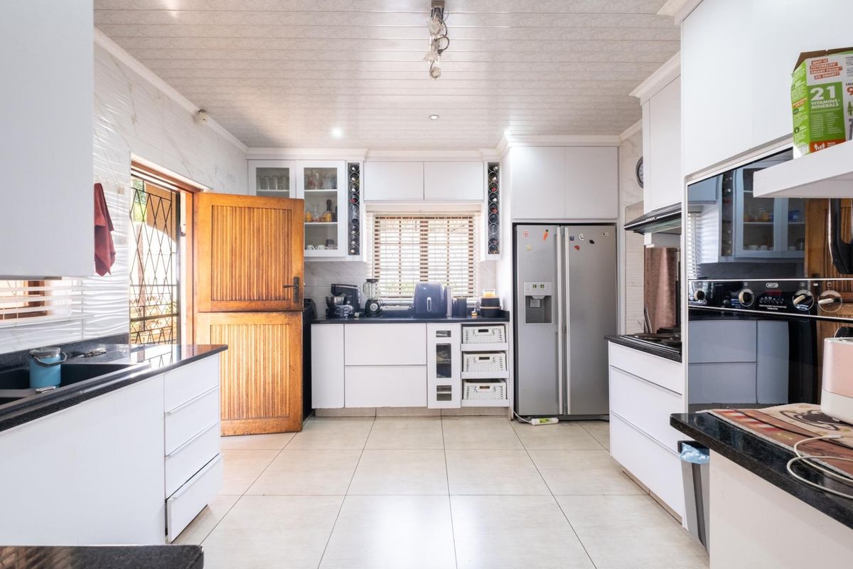 Modern kitchen featuring white cabinetry, black granite countertops, tiled flooring, and integrated appliances, with direct access to the exterior.