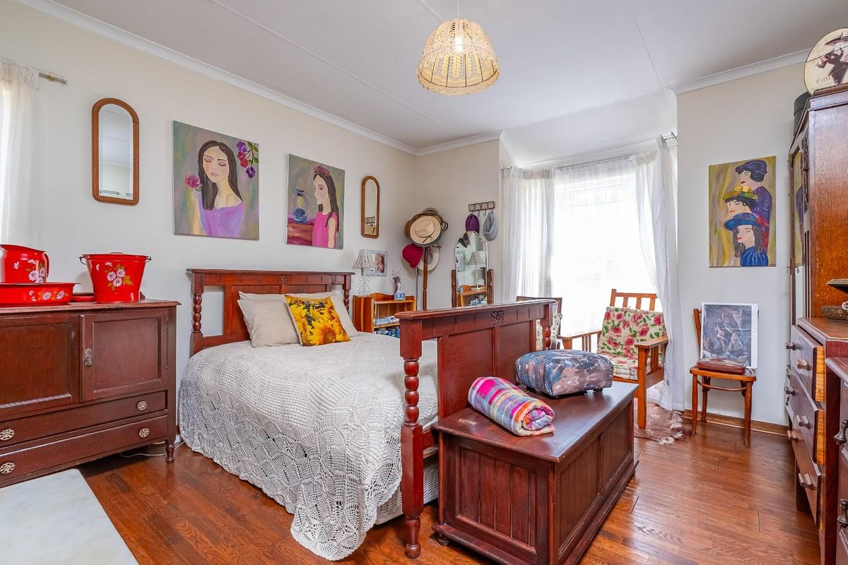 A well-lit bedroom featuring polished hardwood flooring, a bay window with natural light, and classic crown molding.