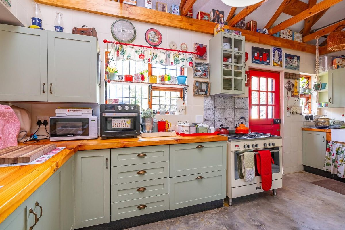 A charming rustic kitchen featuring sage green cabinetry, wooden countertops, a farmhouse-style sink, and exposed timber ceiling beams.