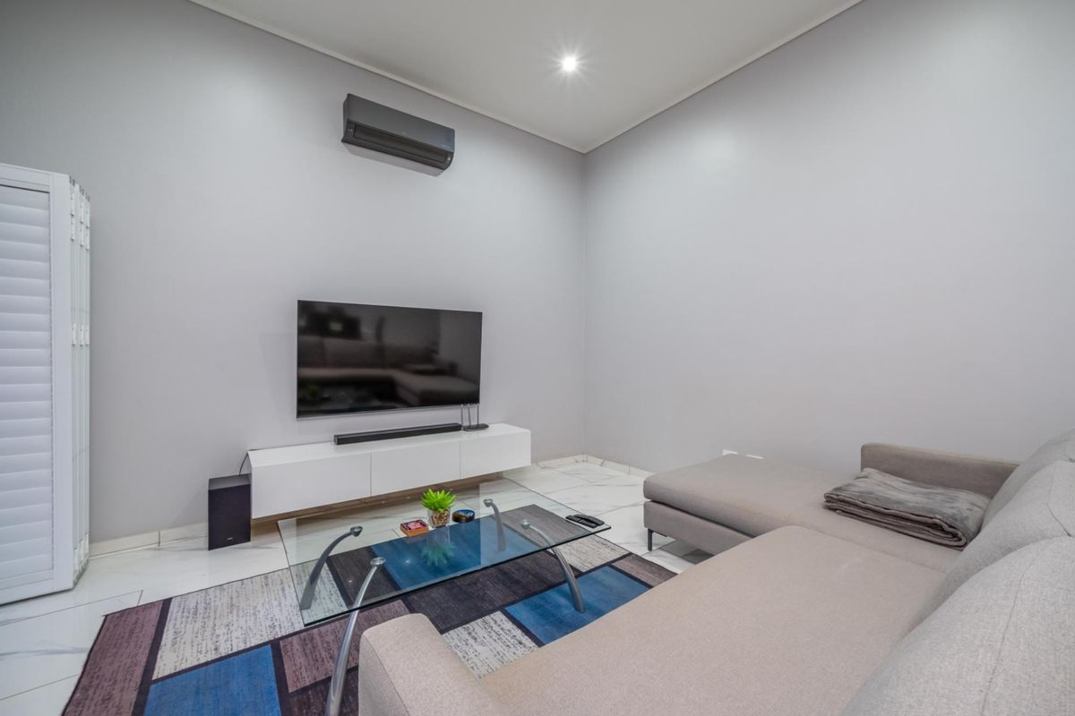 A modern living room featuring sleek white tiled flooring, recessed ceiling lighting, and a wall-mounted air conditioning unit.
