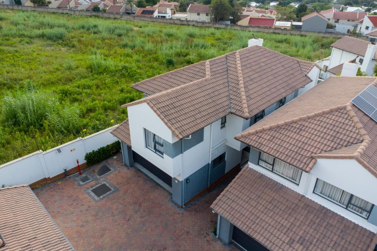 Aerial view of a modern townhouse complex featuring tiled roofs, paved driveways, and perimeter walling.