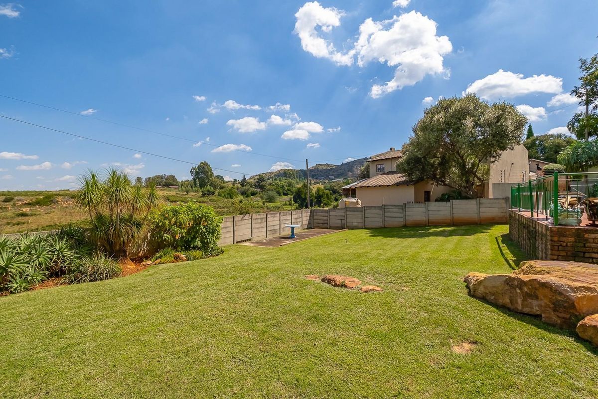 A spacious rear garden featuring a well-maintained lawn, perimeter concrete walling, and scenic views of the surrounding landscape.