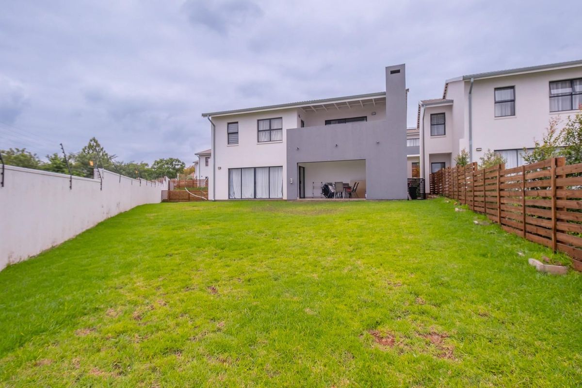 Rear view of the townhouse featuring a spacious lawn, a covered patio with an integrated outdoor fireplace, and secure perimeter fencing.