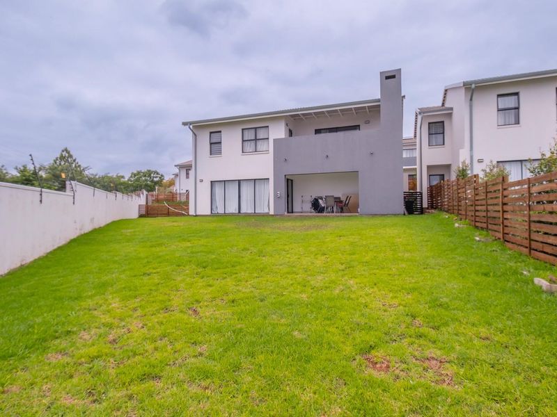 Rear view of the townhouse featuring a spacious lawn, a covered patio with an integrated outdoor fireplace, and secure perimeter fencing.