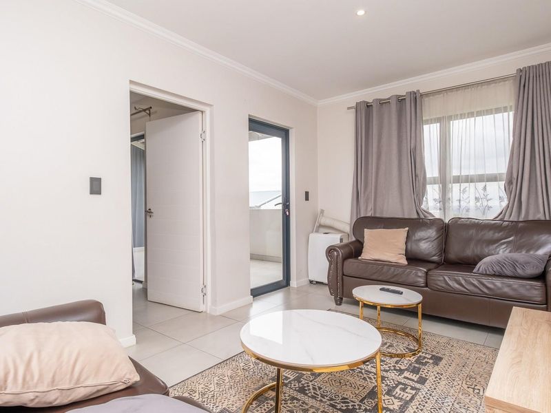 A bright and well-maintained living room featuring neutral tiled flooring, recessed lighting, and direct access to an outdoor balcony area.