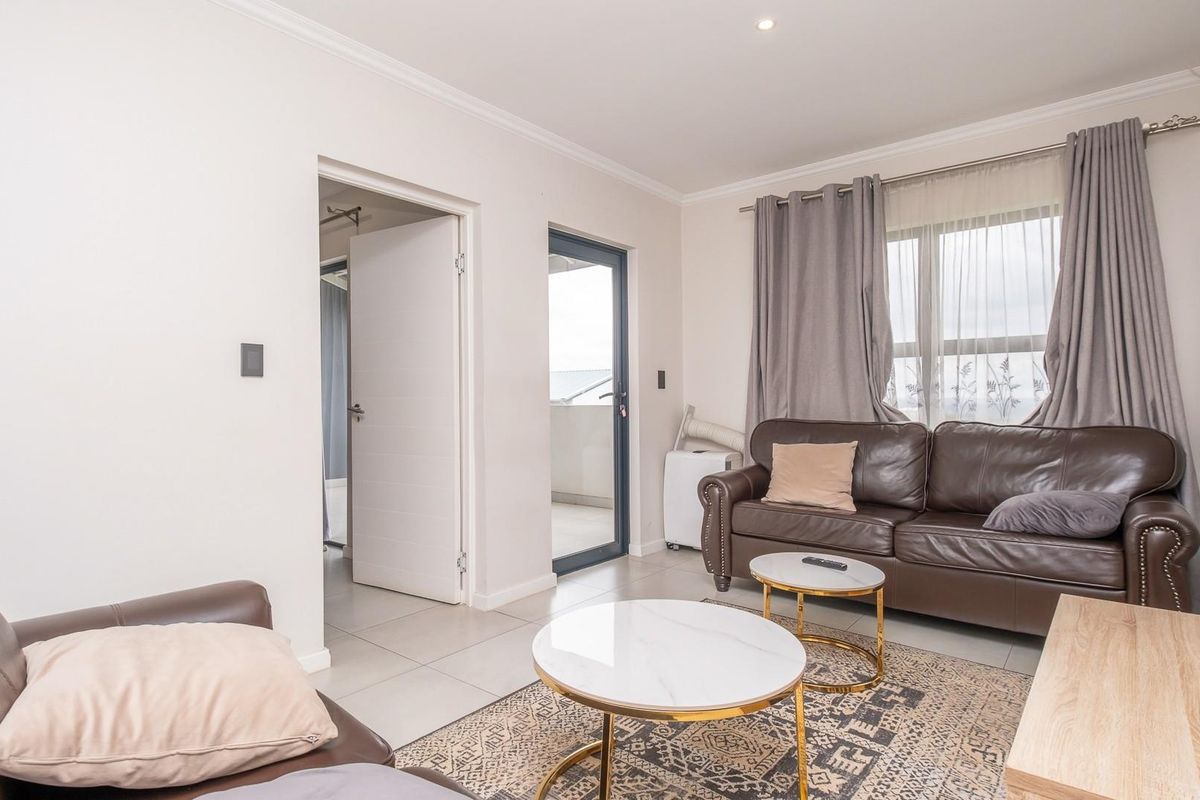 A bright and well-maintained living room featuring neutral tiled flooring, recessed lighting, and direct access to an outdoor balcony area.