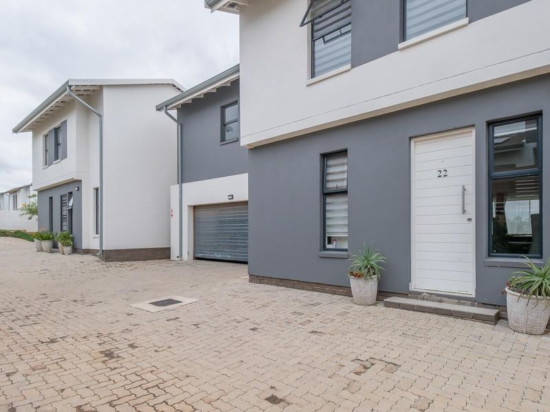 Modern townhouse exterior featuring a paved driveway, roller garage door, and contemporary grey and white facade with aluminium window frames.