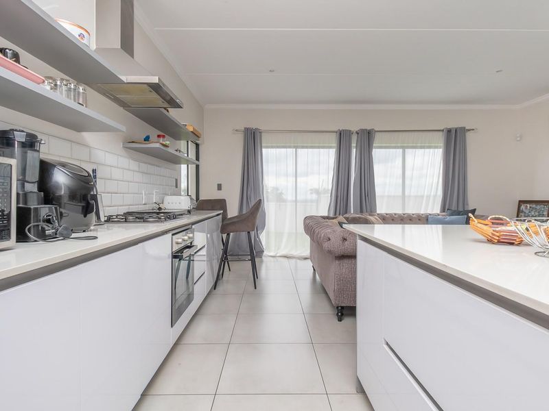 Modern open-plan kitchen and living area featuring sleek white cabinetry, stone countertops, a gas hob, and direct access to a patio through sliding doors.