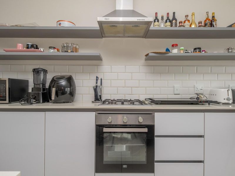 Modern kitchen featuring a gas hob, built-in oven, stainless steel extractor fan, subway tile backsplash, and sleek floating shelving with stone countertops.