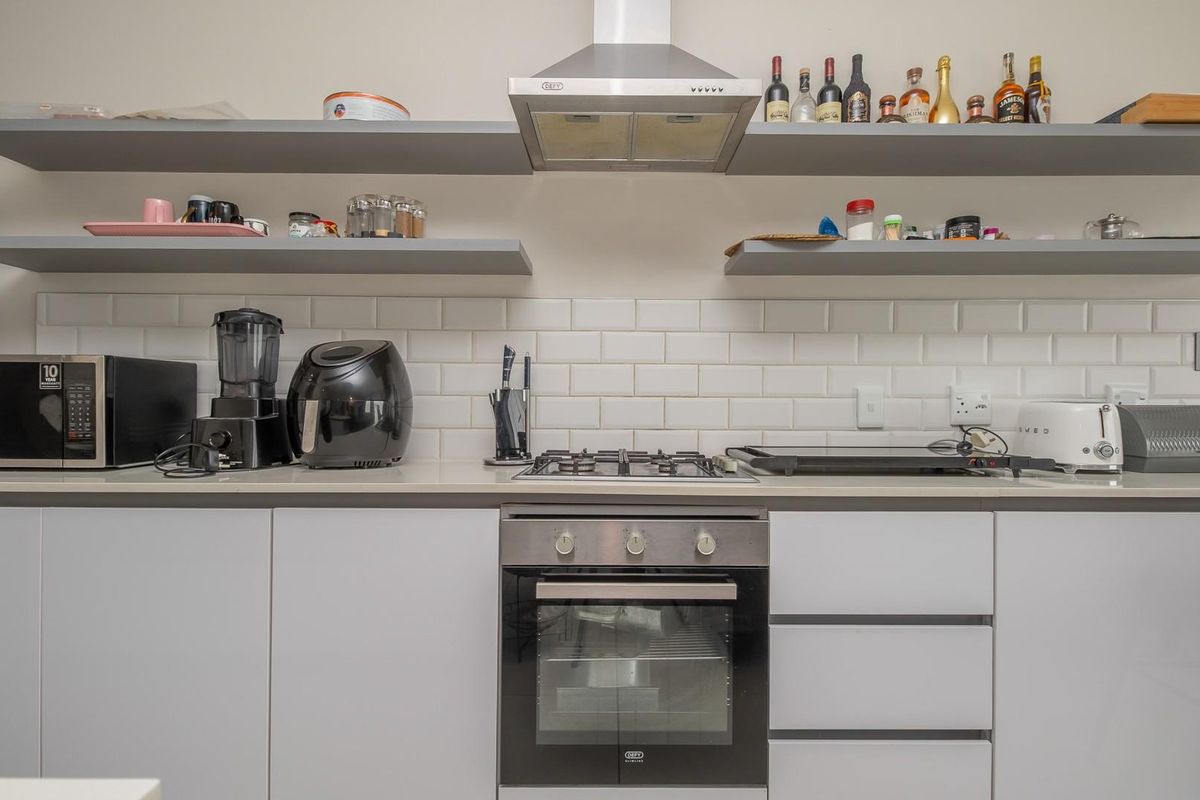 Modern kitchen featuring a gas hob, built-in oven, stainless steel extractor fan, subway tile backsplash, and sleek floating shelving with stone countertops.