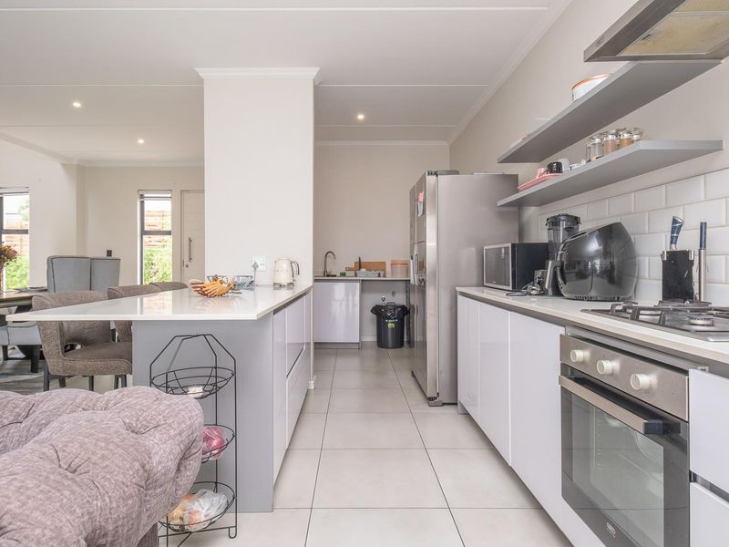 Modern open-plan kitchen featuring a central island, built-in oven, gas hob, subway tile backsplash, and sleek cabinetry, seamlessly flowing into the dining area.
