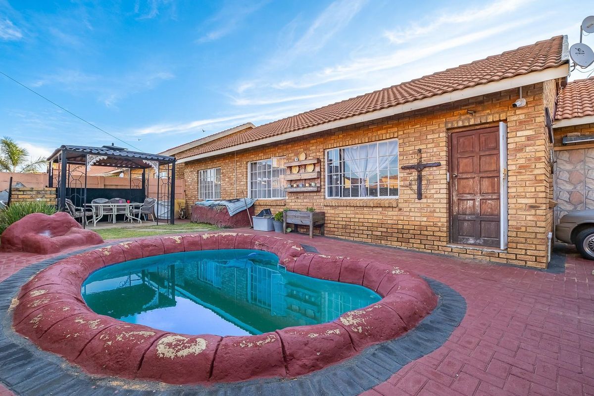 Rear exterior view featuring a brick house, a kidney-shaped swimming pool with a paved surround, and a covered patio area.