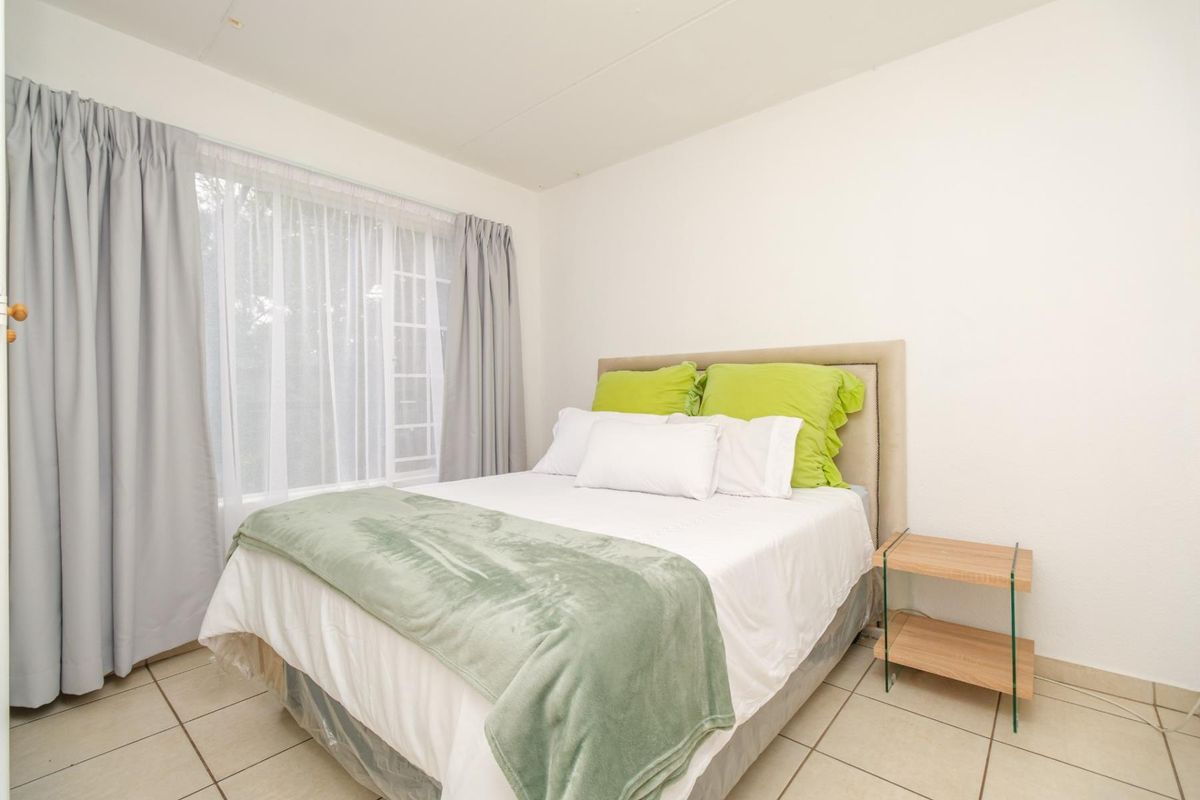 A bedroom featuring tiled flooring and a large window with curtains, providing natural light to the space.