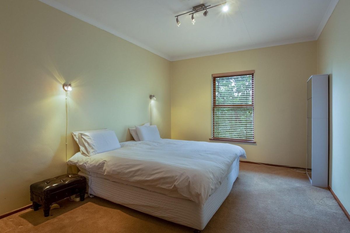 A spacious bedroom featuring neutral wall tones, carpeted flooring, and a window fitted with wooden blinds, providing a comfortable and functional living space.