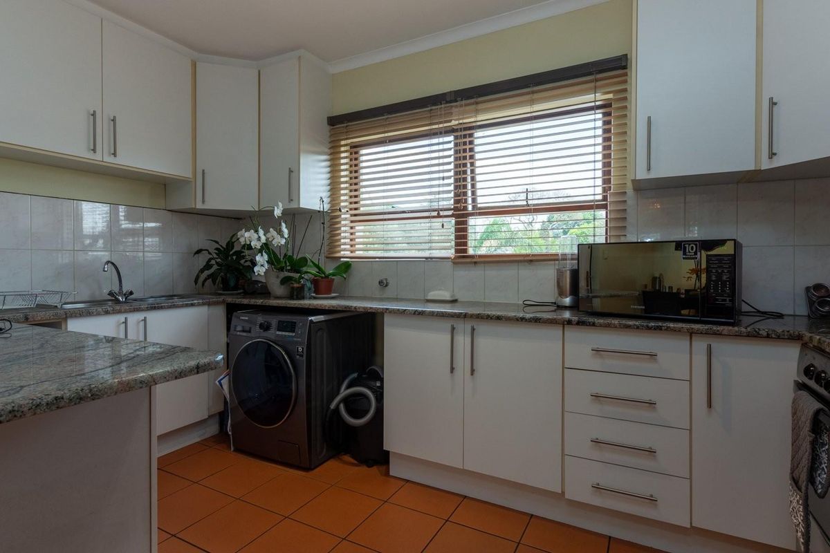 A functional kitchen featuring white cabinetry, granite countertops, tiled backsplash, and a built-in oven with an integrated washing machine space.