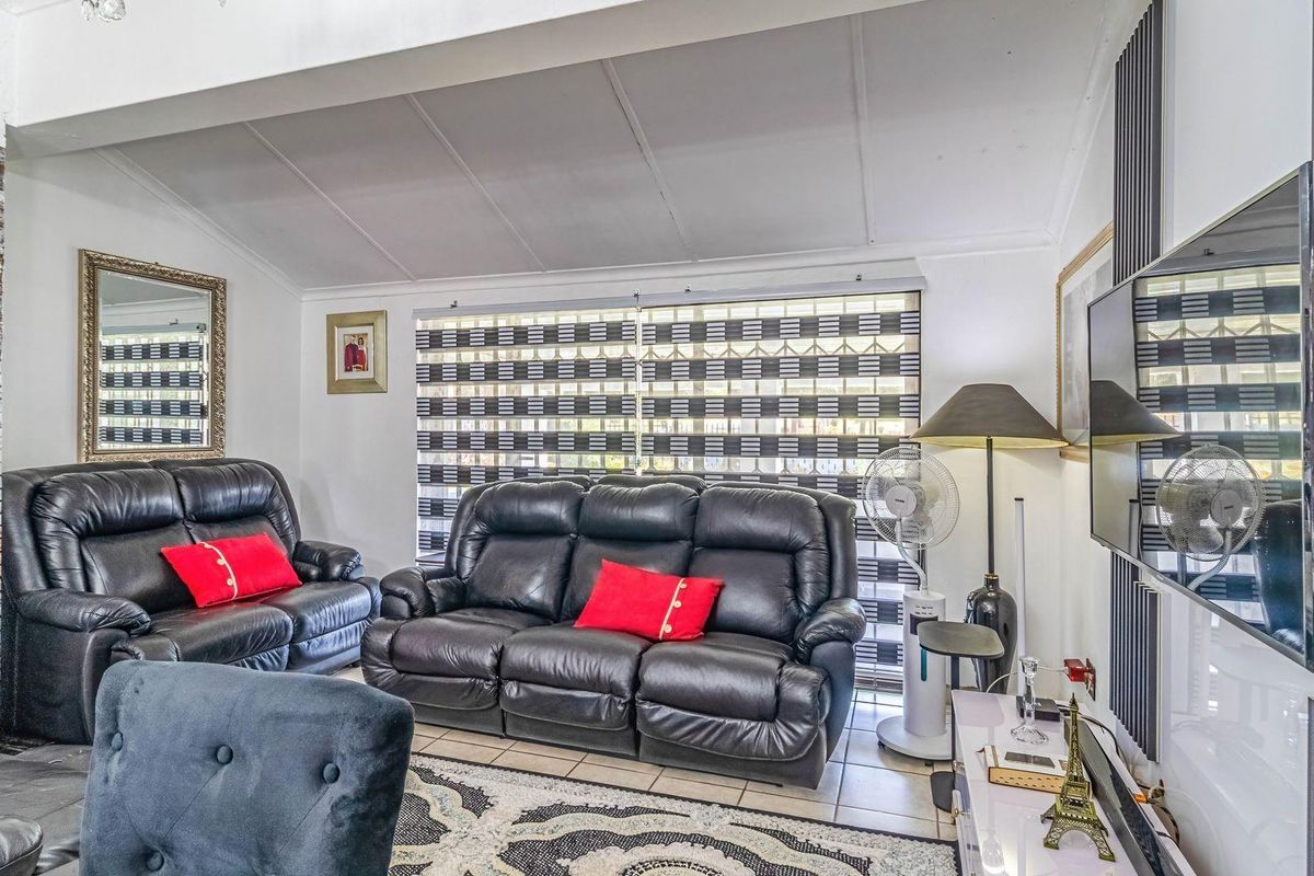 A comfortable living room featuring a brick-accented fireplace, tiled flooring, and large windows with modern zebra blinds, creating a bright and functional space.