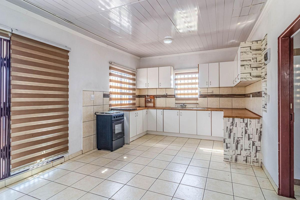 A functional kitchen featuring white cabinetry, wood-look countertops, tiled flooring, and a built-in stove, offering a clean and practical workspace.