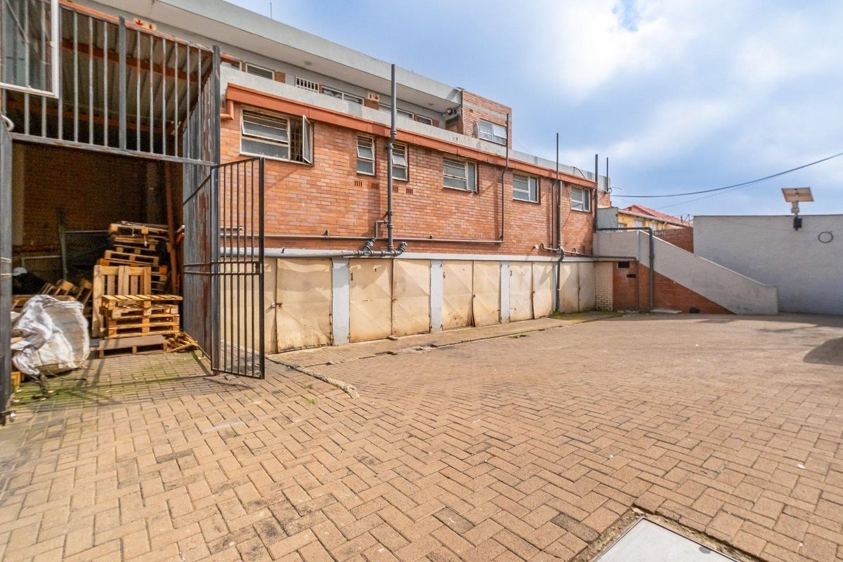 Rear exterior view of the apartment building featuring a paved courtyard area, multiple garage units, and exposed brick facade.