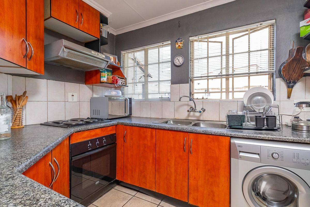 A functional kitchen featuring wood-veneer cabinetry, granite-look countertops, a built-in oven with hob, extractor fan, and integrated space for a washing machine.