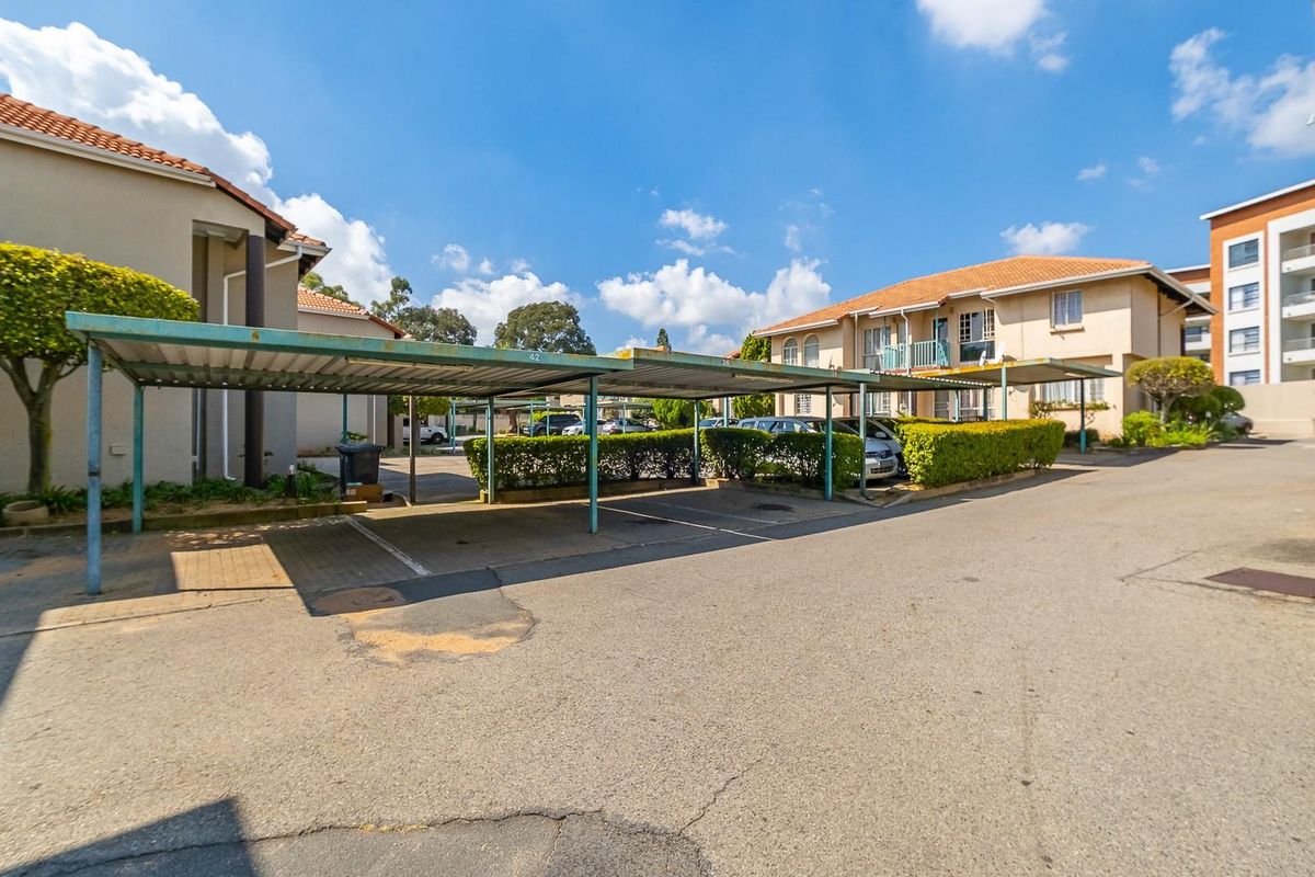 Exterior view of the apartment complex parking area featuring covered carports, paved driveway, and landscaped hedging.