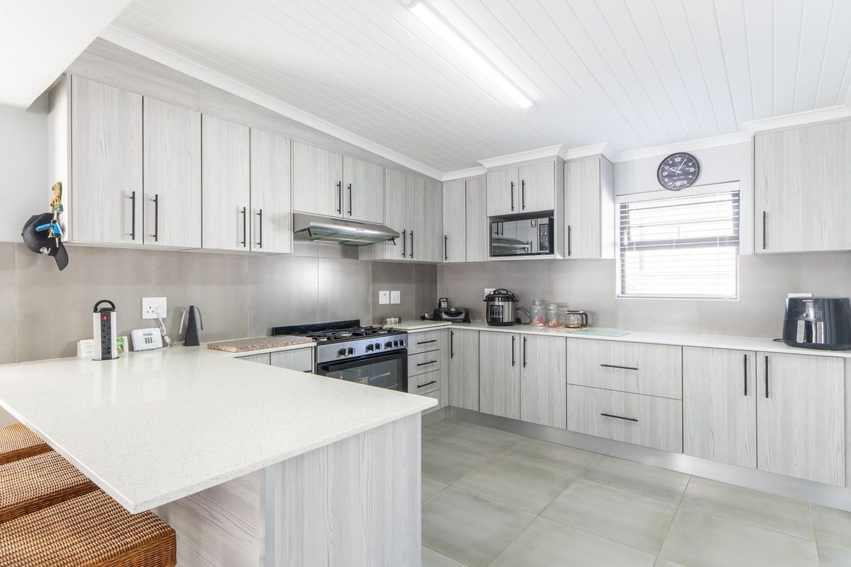 Modern kitchen featuring light wood-grain cabinetry, stone countertops, a gas hob with extractor fan, and tiled flooring.