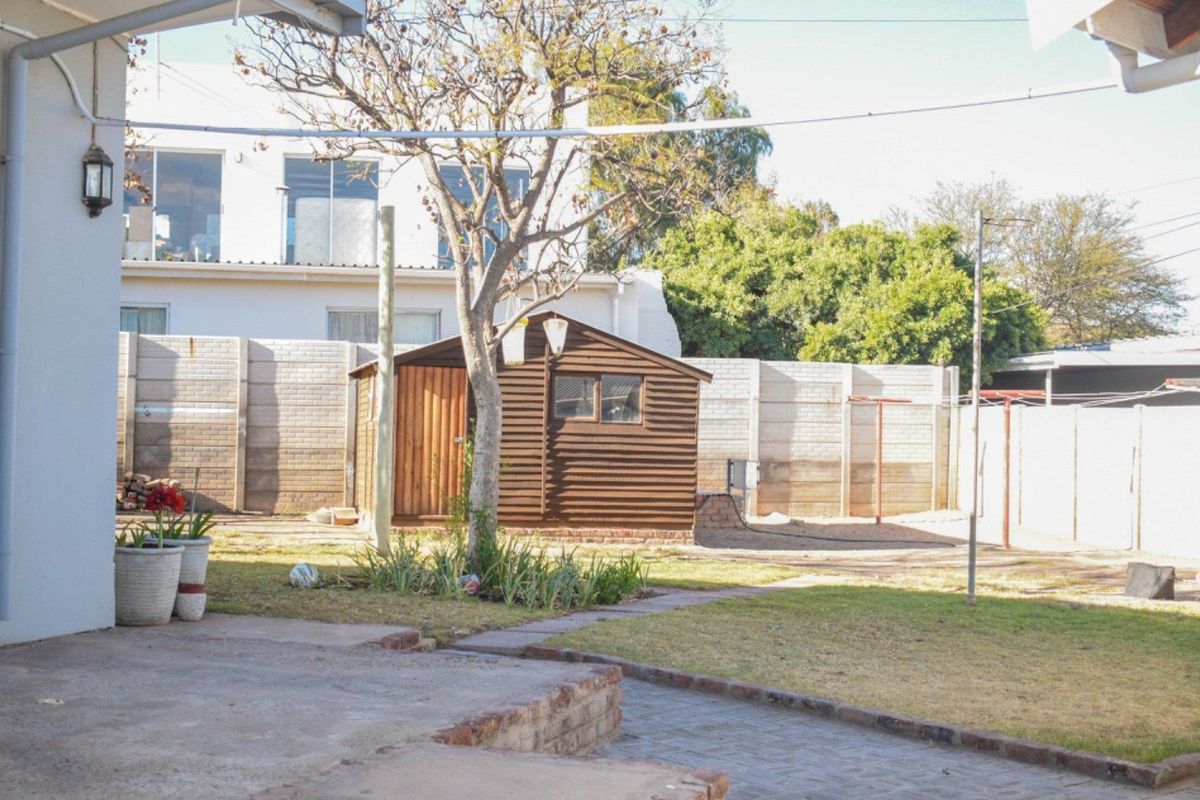 A rear garden view featuring a paved patio area, a small wooden storage shed, and a perimeter boundary wall.