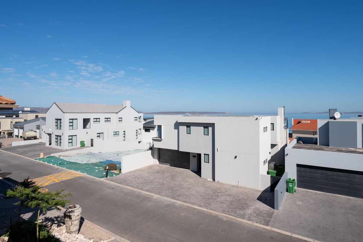 Elevated view of a modern residential street featuring contemporary multi-story homes with paved driveways and coastal surroundings.