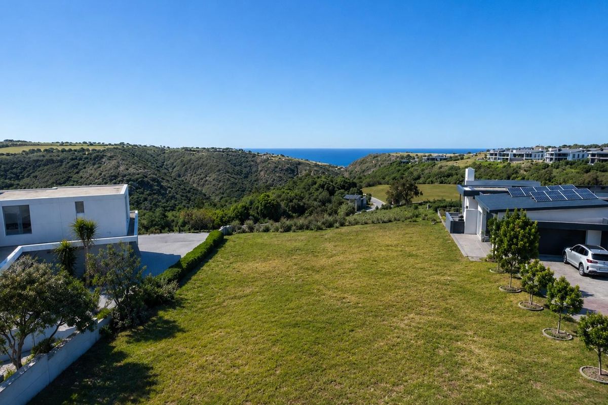 Aerial view of a residential vacant land plot featuring established landscaping, paved driveway access, and scenic coastal views.