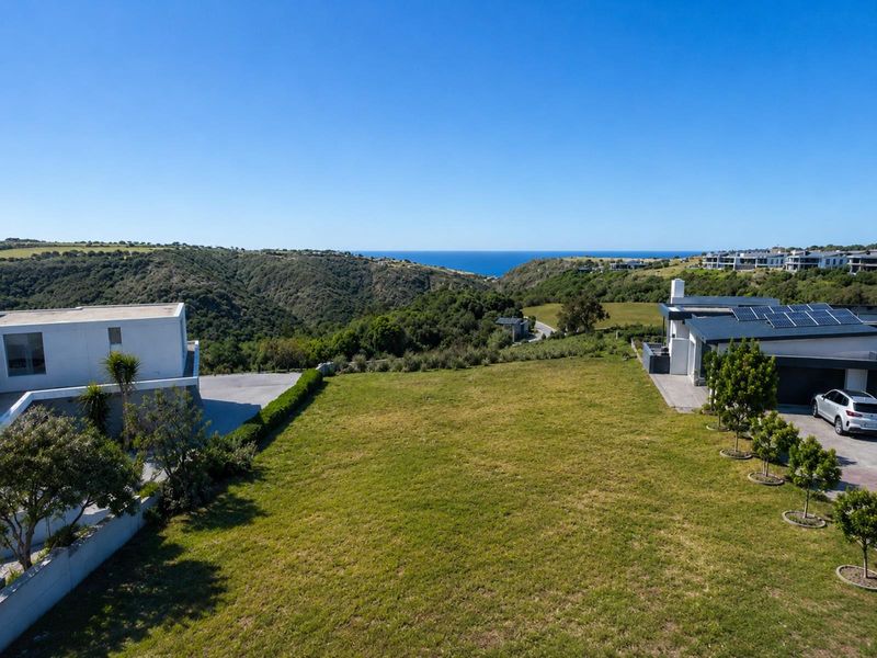 Aerial view of a residential vacant land plot featuring established landscaping, paved driveway access, and scenic coastal views.