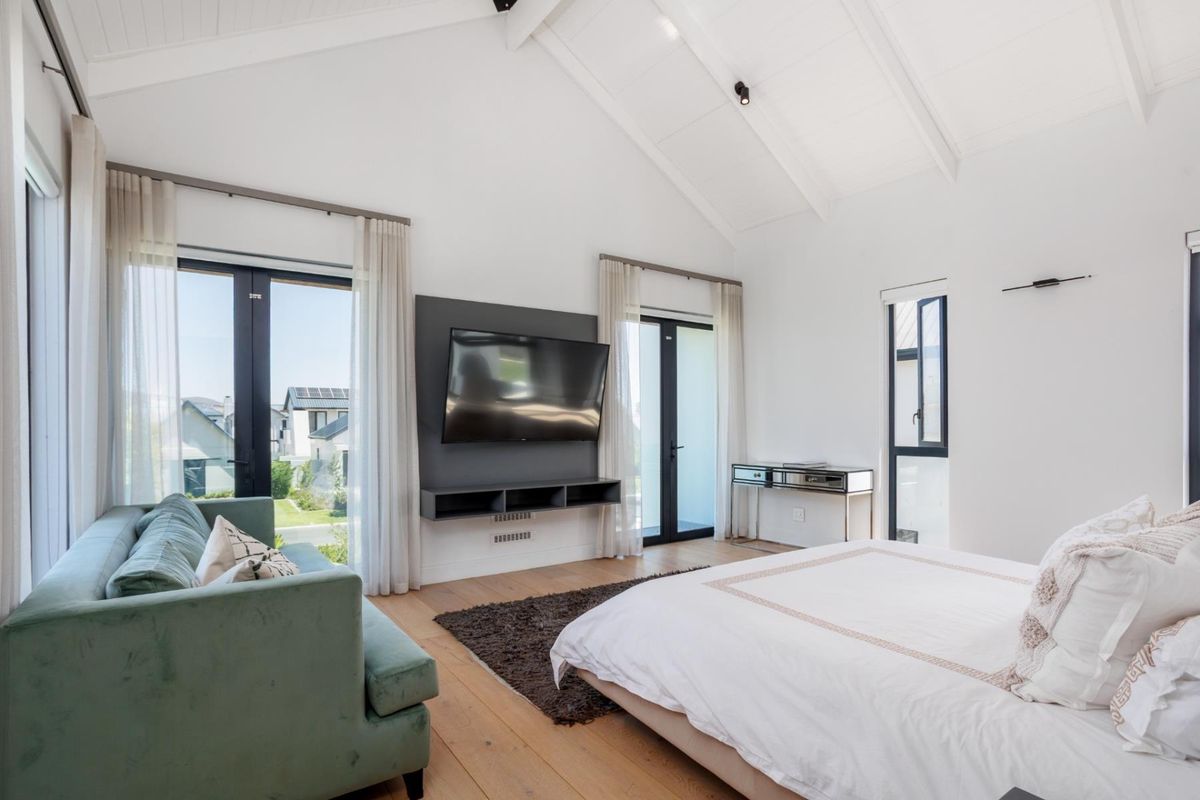 Spacious bedroom featuring high vaulted ceilings, light timber flooring, and dual glass doors providing access to the exterior.