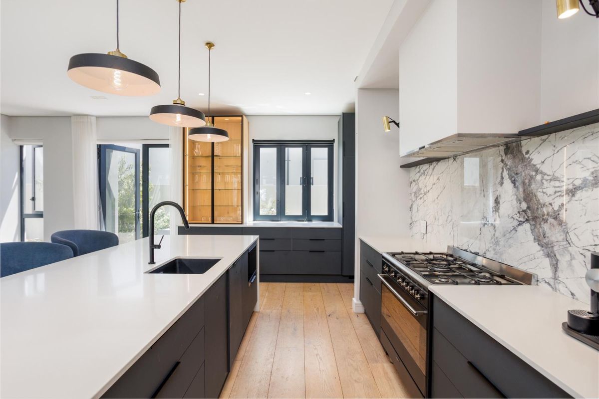 Modern kitchen featuring a large central island, marble-style backsplash, gas range, integrated cabinetry, and high-quality timber flooring with direct access to the patio.