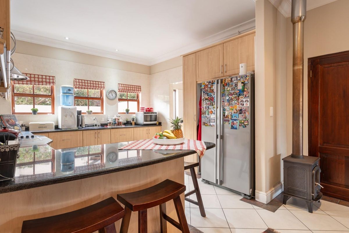 Functional kitchen featuring light wood cabinetry, granite countertops, a breakfast bar, and a freestanding wood-burning fireplace.