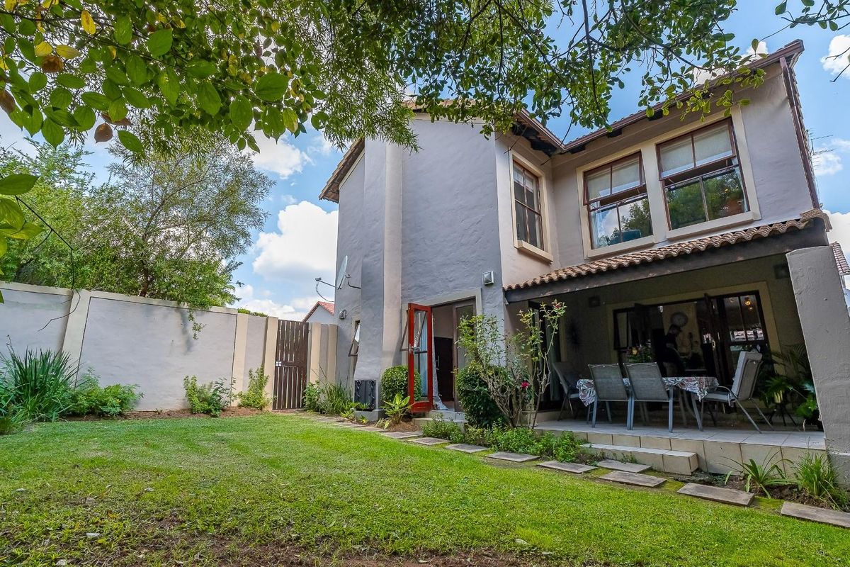Rear view of the two-story house featuring a covered patio, landscaped garden, and perimeter walling.
