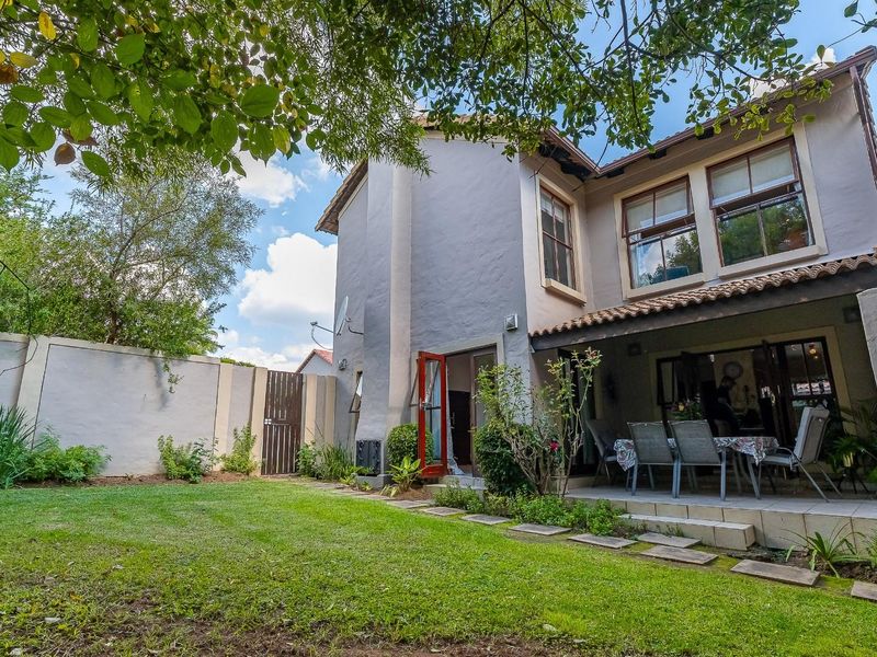 Rear view of the two-story house featuring a covered patio, landscaped garden, and perimeter walling.