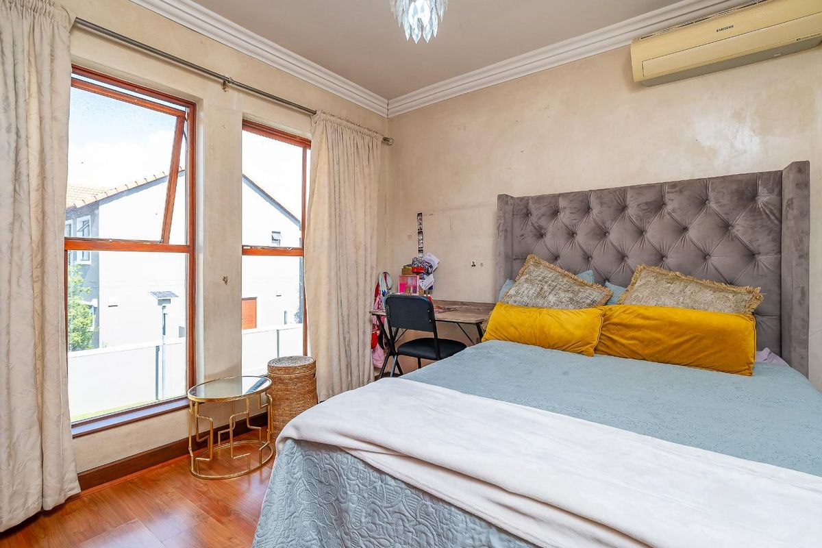 A bedroom featuring timber flooring, crown molding, and a wall-mounted air conditioning unit, offering natural light through large windows.