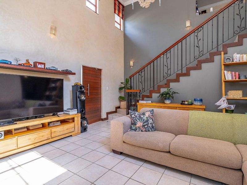 Spacious living room featuring high ceilings, tiled flooring, and a prominent staircase with decorative wrought iron railings.