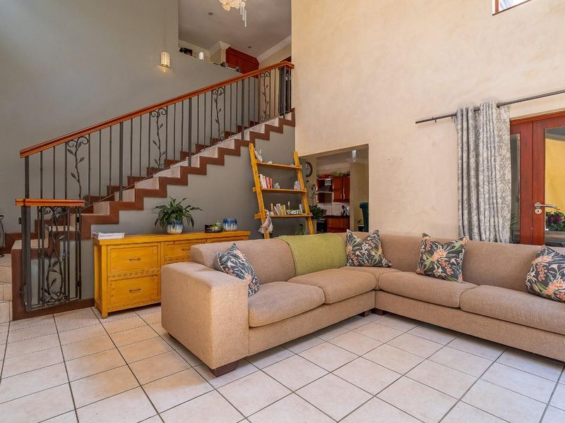 Spacious living area featuring a double-volume ceiling, tiled flooring, and a decorative wrought iron staircase leading to the upper level.