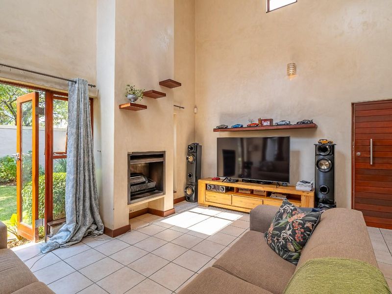 Spacious living room featuring high ceilings, a built-in fireplace, tiled flooring, and large glass doors providing direct access to the garden.